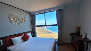 A hotel room with a large bed, a desk, and a view of the beach. - APEC CHAMPA MUI NE BINH THUAN CONDOTEL (Tuy Hoa)