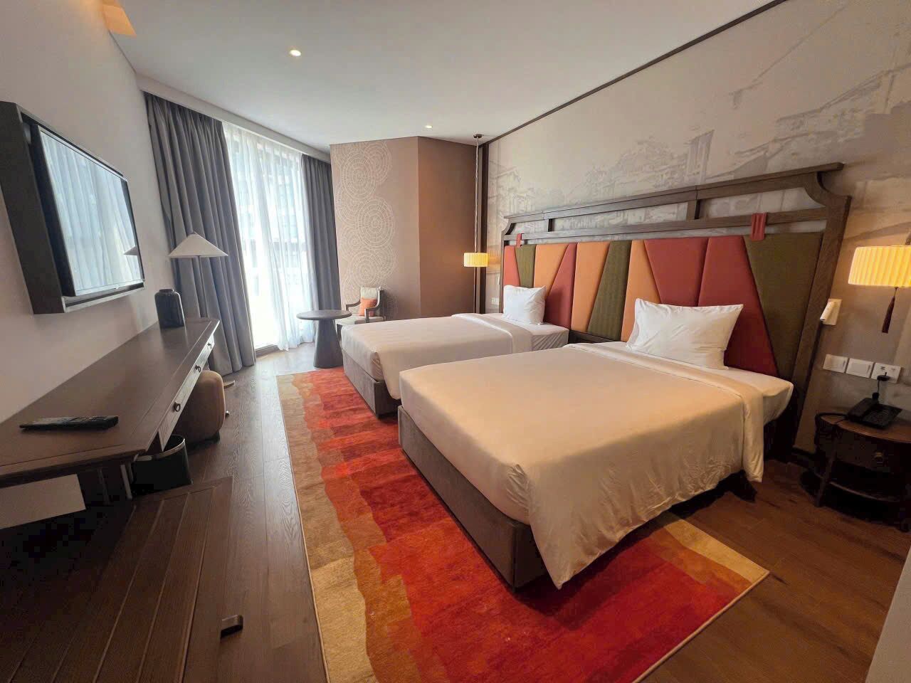 A hotel room with two beds, a desk, and a TV.