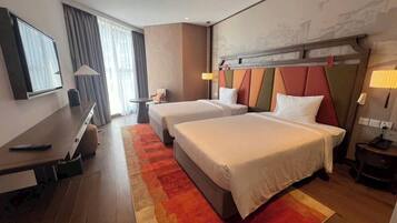 A hotel room with two beds, a desk, and a TV.