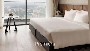 A spacious hotel room with a large bed, a small side table, and a view of the city through a large window. - APEC CHAMPA MUI NE BINH THUAN CONDOTEL (Tuy Hoa)