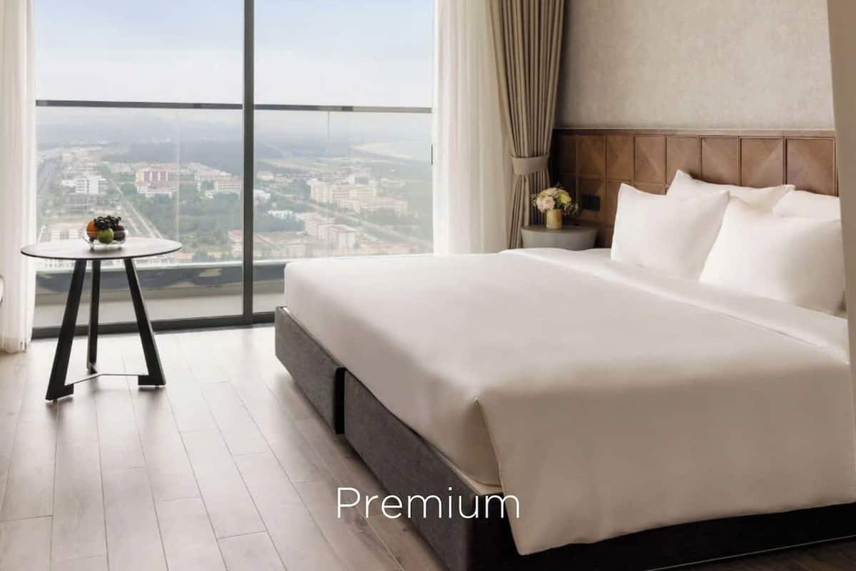 Ein geräumiges Hotelzimmer mit einem großen Bett, einem kleinen Beistelltisch und Blick auf die Stadt durch ein großes Fenster.