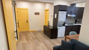A compact living space with a kitchenette, a sofa, and a wooden floor. - Rocky Ridge Retreat — Your Gateway to the Rockies (Calgary)