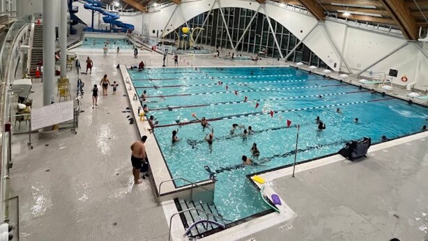 An indoor swimming pool with multiple lanes, a water slide, and a high arched ceiling. - Rocky Ridge Retreat — Your Gateway to the Rockies (Calgary)