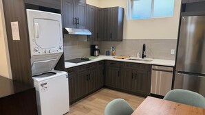 A compact kitchen with dark wood cabinets, a stainless steel refrigerator, a built-in oven, and a coffee maker. - Rocky Ridge Retreat — Your Gateway to the Rockies (Calgary)