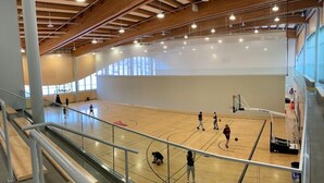 A basketball court with a high ceiling and wooden beams, a basketball hoop, and a spectator area with a railing. - Rocky Ridge Retreat — Your Gateway to the Rockies (Calgary)