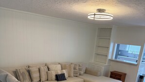 Ein modernes Wohnzimmer mit einem Ecksofa, Holzboden, einer eingebauten Vitrine und einem Fenster mit Blick.