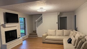Ein Wohnzimmer mit Kamin, einer Treppe, einem beigen Sofa und einem Flachbildfernseher.