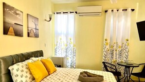 A room with a bed, a small table, a chair, a window with curtains, and wall art. - Room-hotel Maria Bonita Higüey 2 (Higuey)