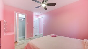 Camera da letto con pareti rosa, un letto, una ventola a soffitto e un cabina armadio.