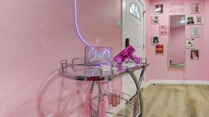 Una stanza rosa con un tavolo in vetro, un neon e diverse immagini incorniciate alle pareti.