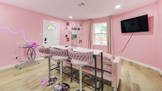 Una camera decorata in rosa con una TV, un tavolo e due sedie.