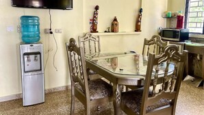 A dining area with a glass table and wooden chairs, a water dispenser, a television, and a microwave. - Room-hotel Maria Bonita Higüey H301 (Higuey)