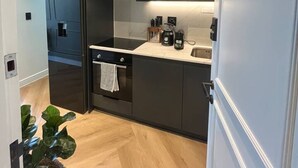 A compact kitchen with dark cabinetry, a built-in oven, a refrigerator, and a countertop with a kettle and coffee maker. - Corner Suite The Valour in De Waterkant (Cape Town)