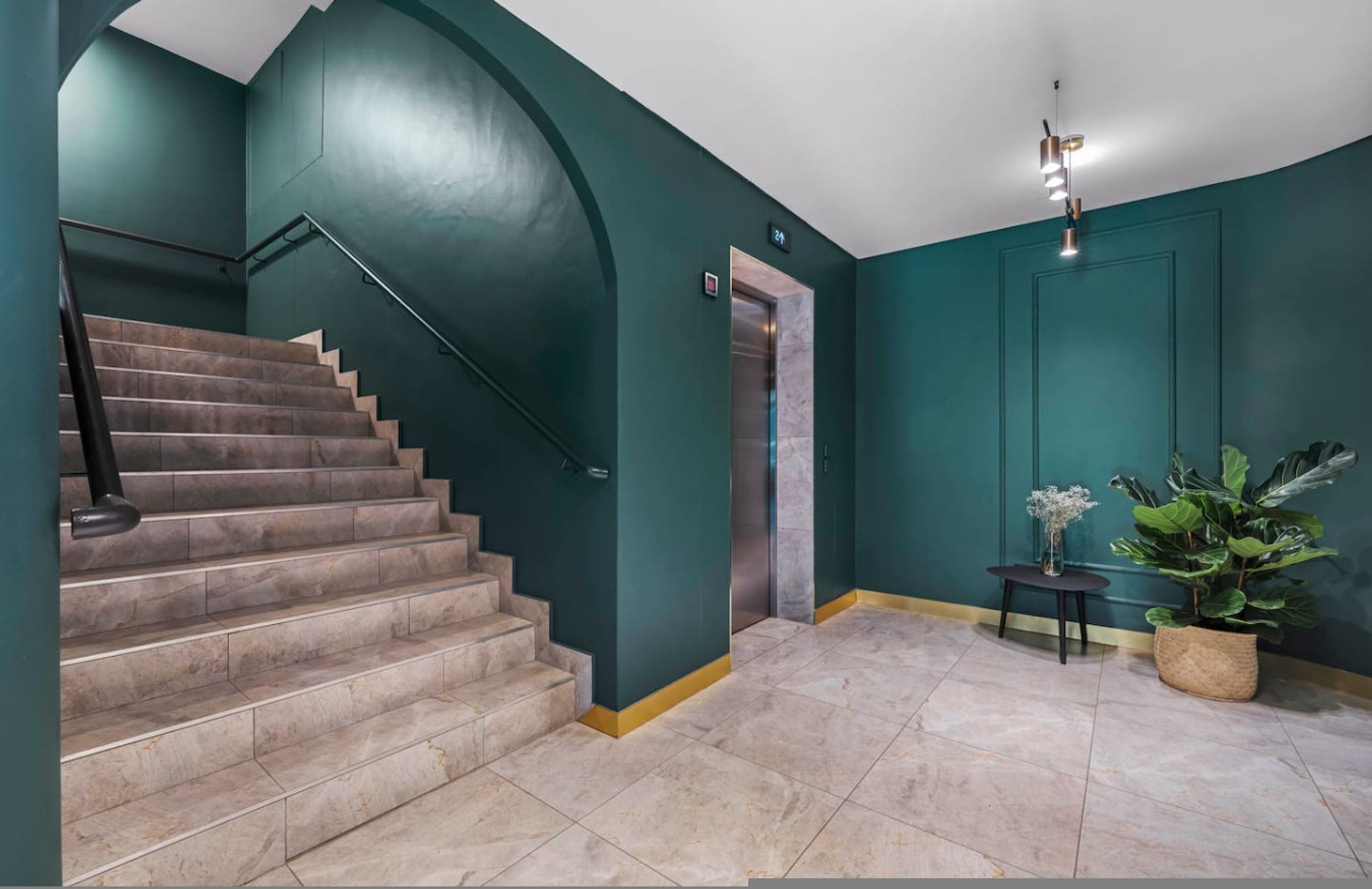Una escalera con barandilla, una puerta con un letrero de número y una planta en maceta.