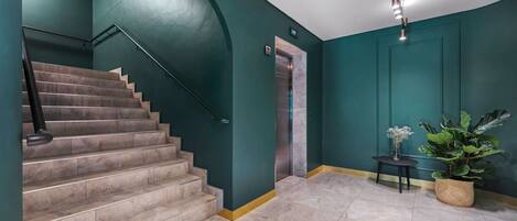 Una escalera con barandilla, una puerta con un letrero de número y una planta en maceta.
