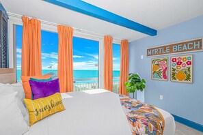 Ein Schlafzimmer mit Bett, orangefarbenen Vorhängen und Blick auf den Ozean. Auf dem Schild steht 'Myrtle Beach'.