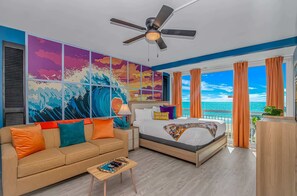 Ein Schlafzimmer mit Bett, einer Couch, einem Deckenventilator, Meerblick und einem großen Gemälde einer Welle an der Wand.