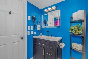 Ein Badezimmer mit blauer Wand, weißer Tür und einem Waschbecken mit Spiegel darüber.