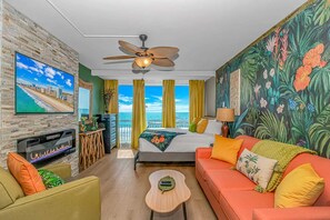 Ein Hotelzimmer mit Bett, Sofa, Fernseher, Deckenventilator und einem Balkon mit Blick.