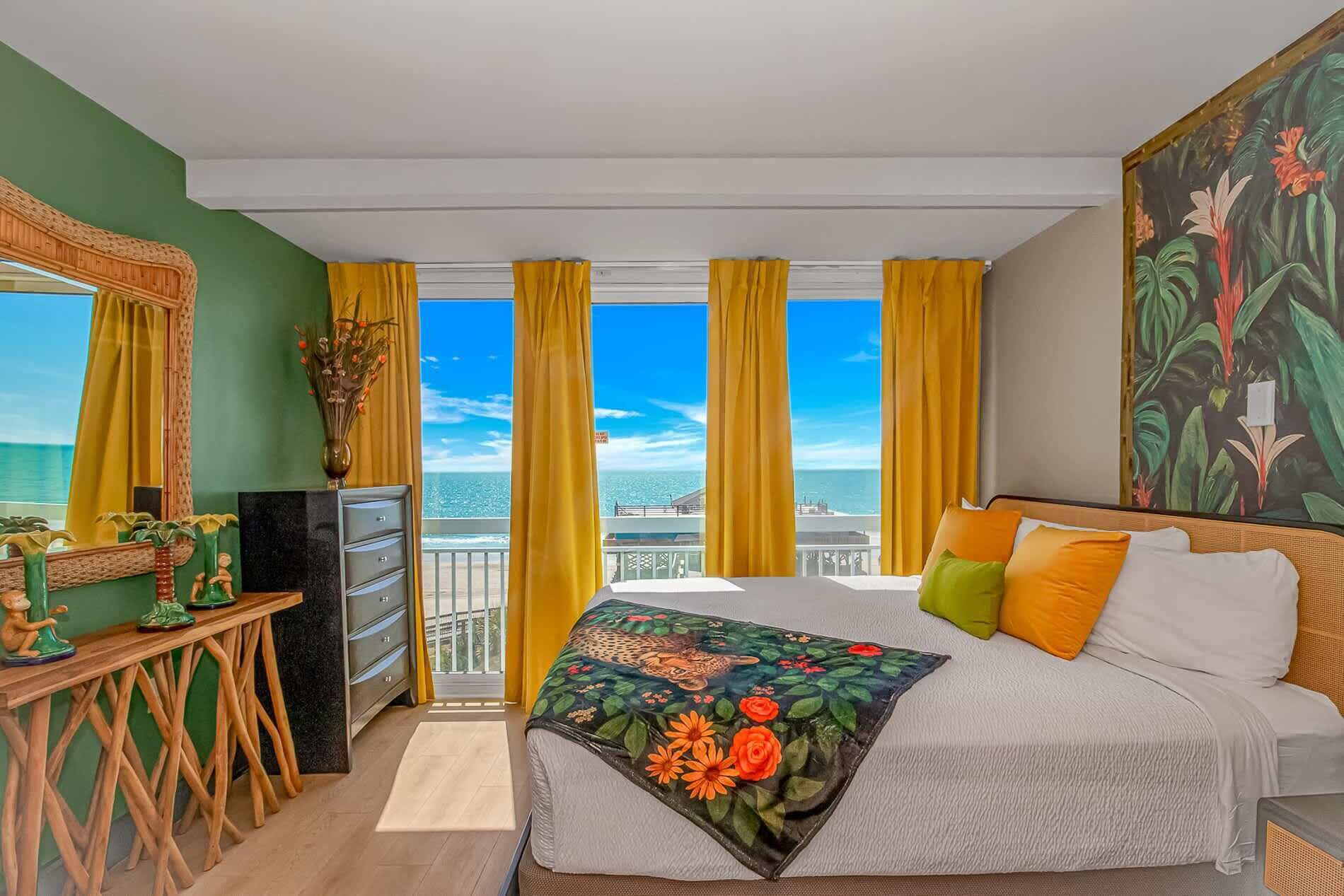 Un dormitorio con cama, cómoda, escritorio y un amplio ventanal con cortinas.