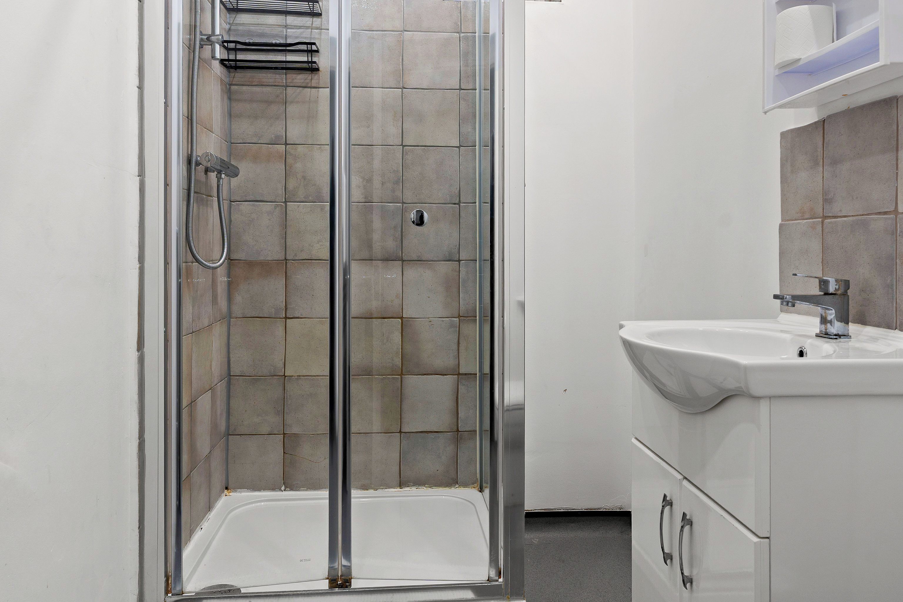 Een douche met glazen deur, een witte wastafel en een betegelde muur.