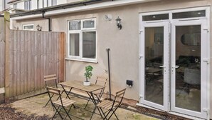 A residential property with a patio, a wooden fence, a table with chairs, a potted plant, and a sliding glass door. - Cosy 2 Bed-5 Guests-Garden-Parking&WiFi (London)