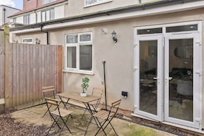A residential property with a patio, a wooden fence, a table with chairs, a potted plant, and a sliding glass door. - Cosy 2 Bed-5 Guests-Garden-Parking&WiFi (London)