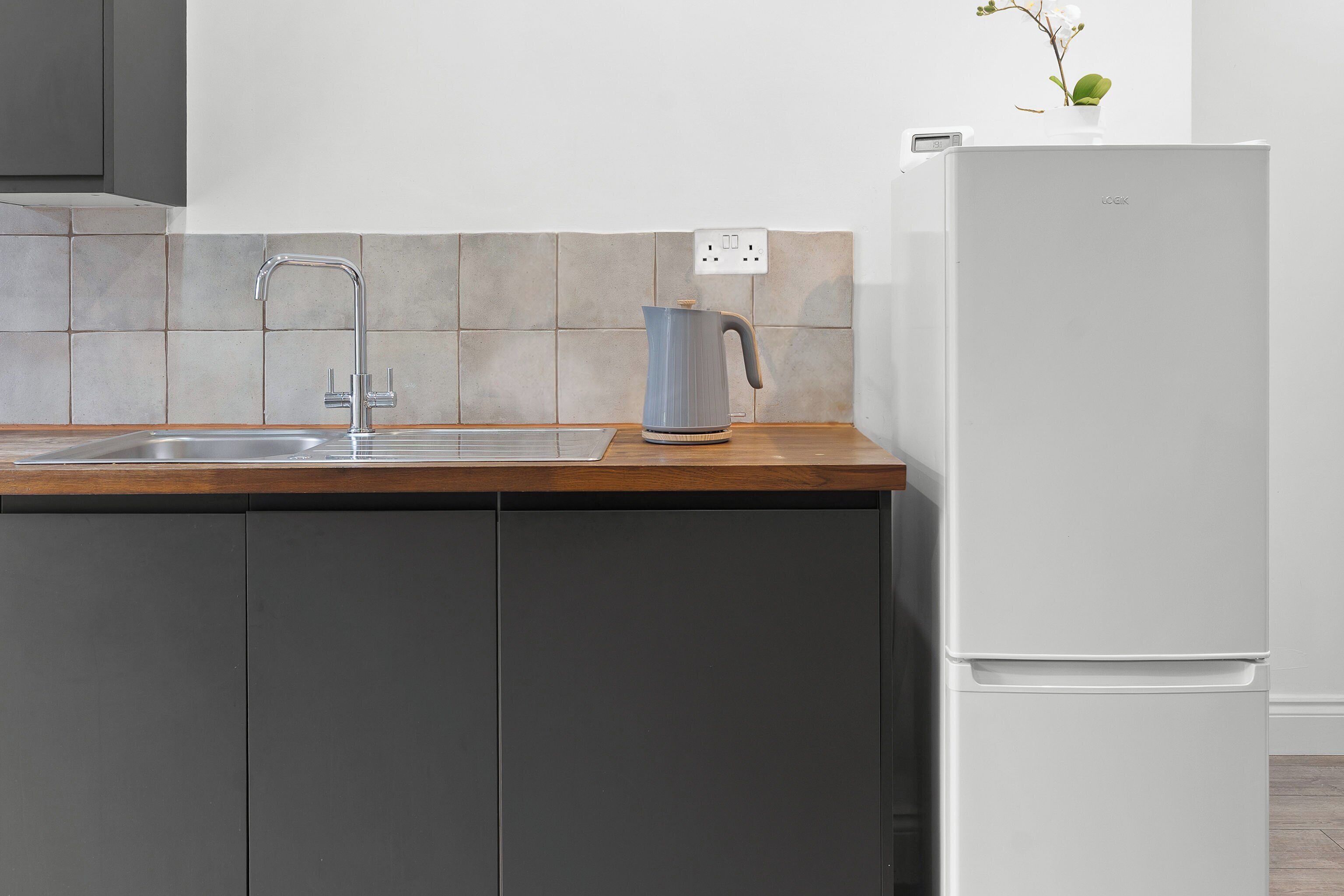 A kitchen with a sink, a kettle, and a white refrigerator.