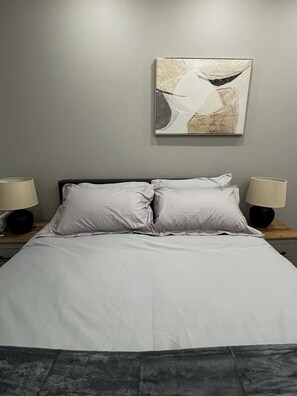 Ein Bett mit weißer Bettwäsche, zwei Nachttischlampen und ein an der Wand hängendes abstraktes Gemälde.
