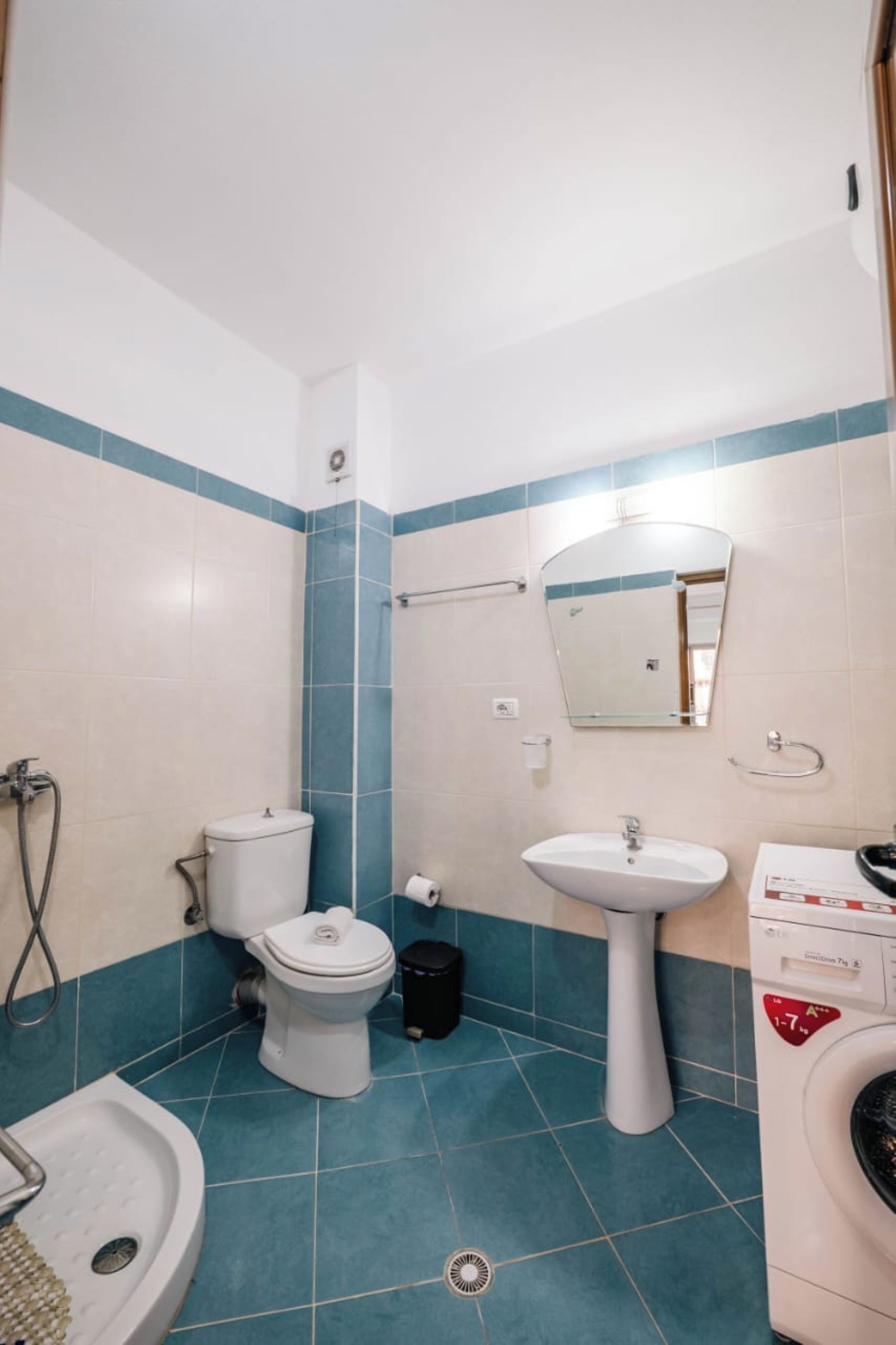 A bathroom with a toilet, sink, mirror, and washing machine.