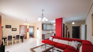 A living room with a red sofa, a glass coffee table, and a dining area with chairs and a table. - Albania Dream Saranda Apartments (Saranda)