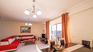 A living room with a red sofa, a dining table with chairs, a TV, and a window with curtains. - Albania Dream Saranda Apartments (Saranda)