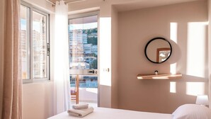 A hotel room with a bed, a window with curtains, a mirror, and a view of buildings. - Albania Dream Saranda Apartments (Saranda)