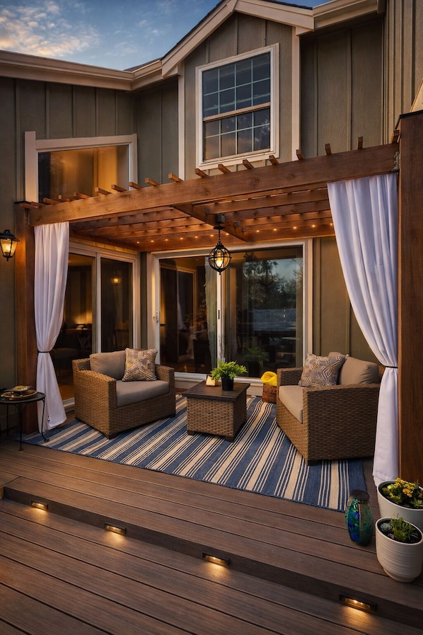 A covered patio with wicker furniture, a wooden deck, and a pergola with string lights.