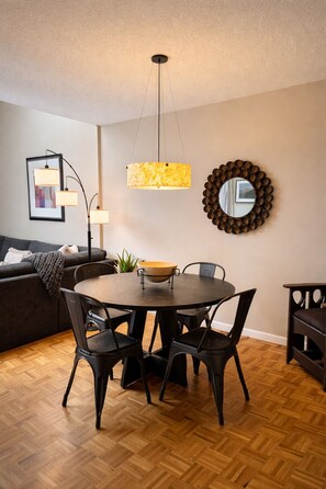 A dining area with a round table, black chairs, a wooden bowl centerpiece, a hanging light fixture, a framed picture, and a mirror on the wall.
