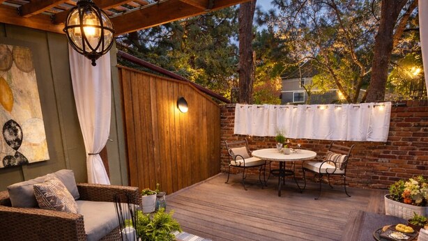 Eine Terrasse im Freien mit Korbmöbeln, einem runden Tisch und einer Pergola.