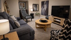 Ein Wohnzimmer mit Sofa, Sessel, Couchtisch, Fernseher und Kunstwerken an den Wänden.