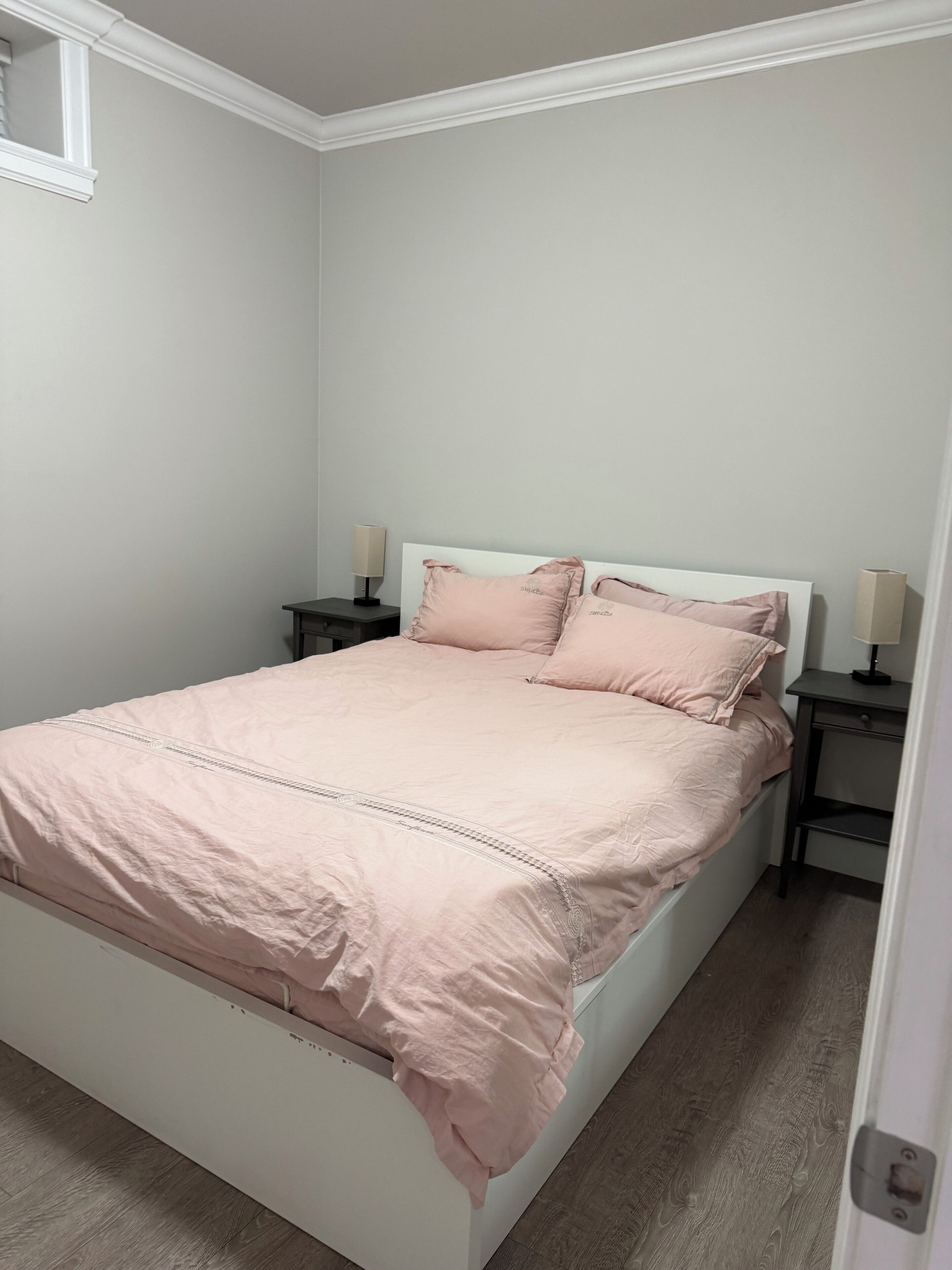 Un lit bien fait, avec une tête de lit blanche, deux tables de chevet avec des lampes et un mur de couleur claire.