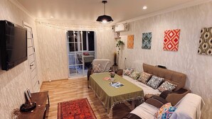 Un salon comprenant un canapé, une table basse, un téléviseur, un coin repas avec une table et des chaises, et un tapis rouge à motifs.