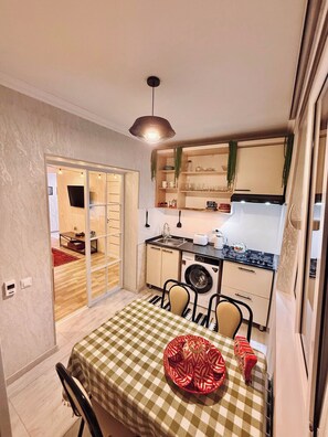 Una cocina compacta con zona de comedor, que incluye una mesa con mantel a cuadros y sillas, lavadora y estufa.