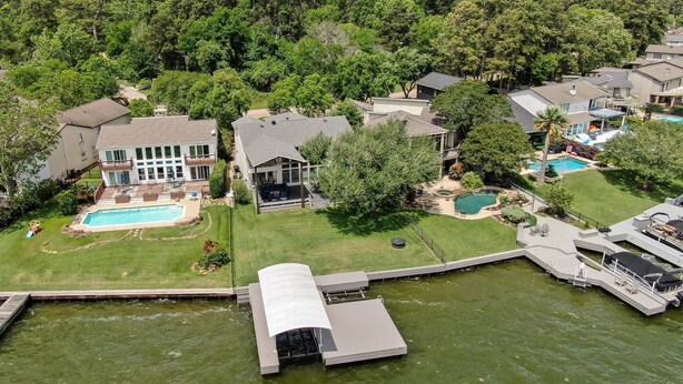 An aerial view of a residential area with multiple houses, a swimming pool, and a dock extending into a body of water. - 5BR Lake Conroe Waterfront | 3 Kings + Private Dock | Swim + Fish | Games + Fire Pit | Sleeps 12 (Montgomery)