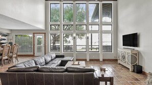 A spacious living room with a large sectional sofa, a flat-screen TV, and a dining area with chairs and a table. - 5BR Lake Conroe Waterfront | 3 Kings + Private Dock | Swim + Fish | Games + Fire Pit | Sleeps 12 (Montgomery)