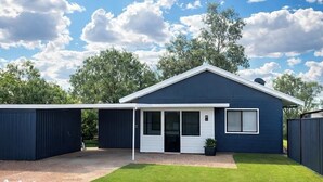 Et moderne hus med en overdækket veranda, en indhegnet have og en klar blå himmel.