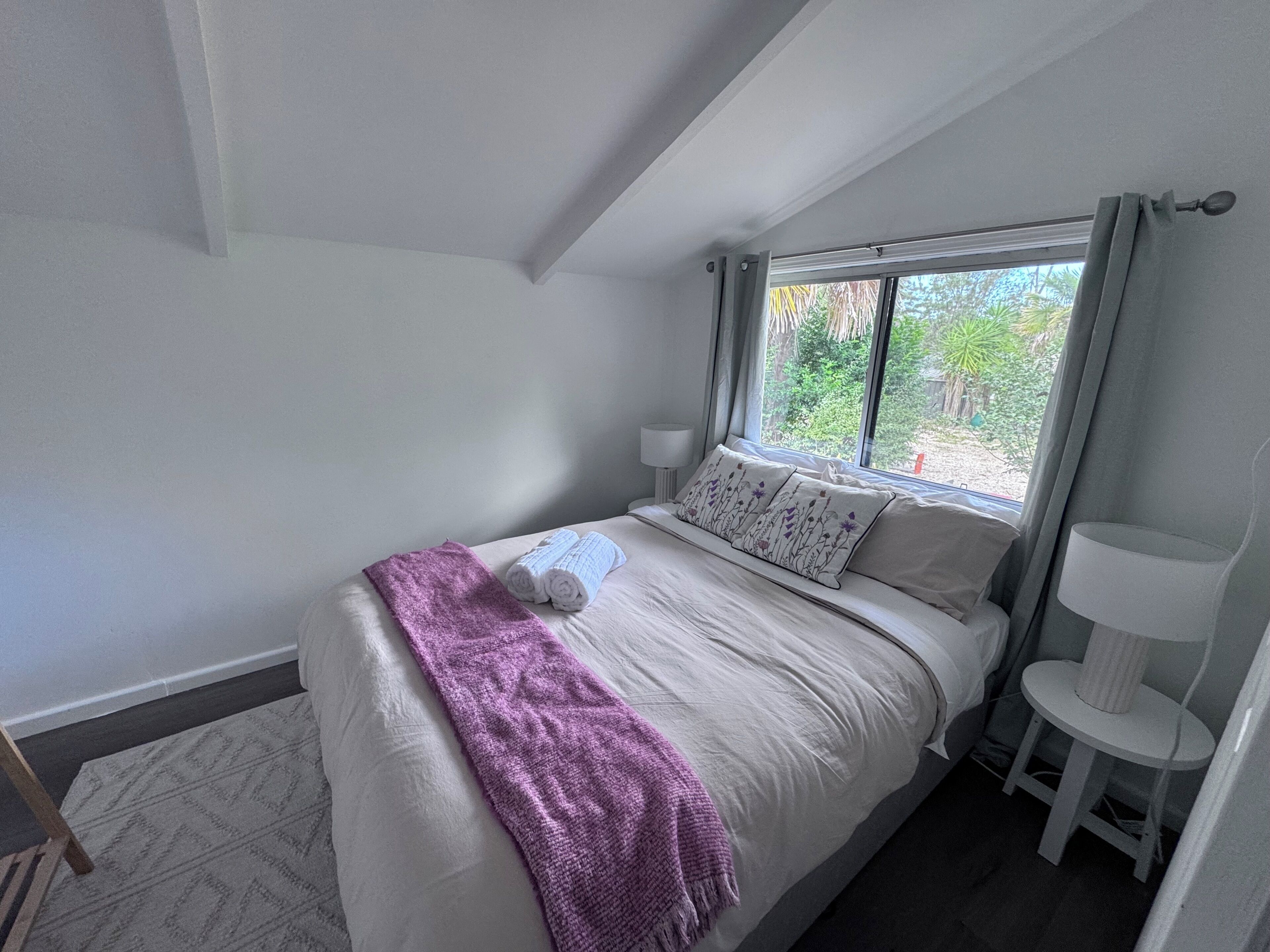 A bedroom with a bed, a window, a lamp, and a chair.