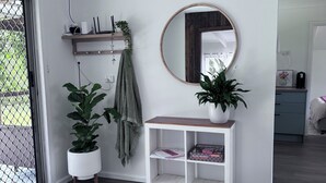Un interior moderno con una consola blanca, un espejo redondo y dos plantas en macetas.