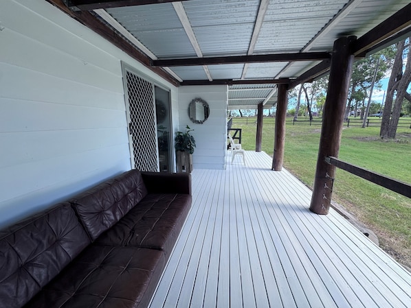 A covered porch with a wooden bench, a metal railing, and a view of a grassy area.