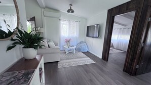 Una sala de estar con un sofá, una mesa de centro, un televisor y un ventanal con cortinas.