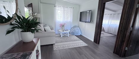 Ett vardagsrum med en soffa, ett soffbord, en tv och ett stort fönster med gardiner.