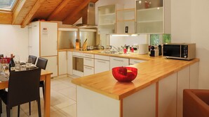 A modern kitchen with wooden beams, a dining area with a table set for two, and a microwave on the counter. - Haus Brigitte, Apartment Dufour (Zermatt)