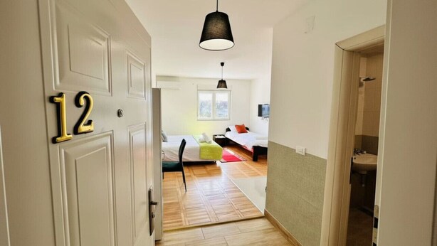 A hallway leading to a bedroom with a bed, a chair, and a hanging light fixture. - Airport Studio-Quick City Access w/ Free Parking (Surčin)
